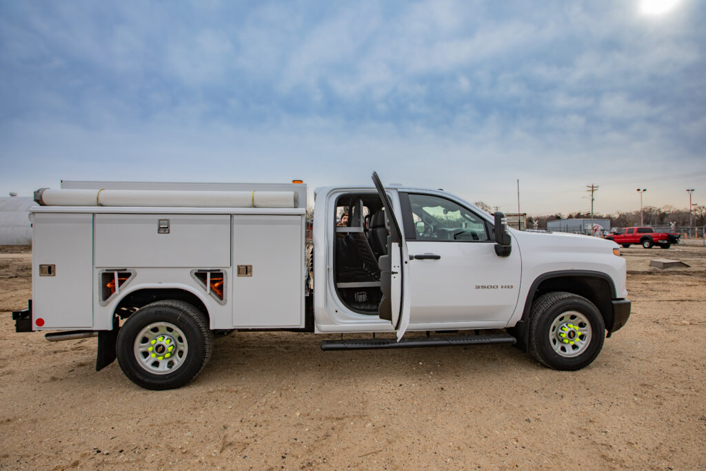 Side view of a white work truck that has the back door open and storage equipment in the back seat.
