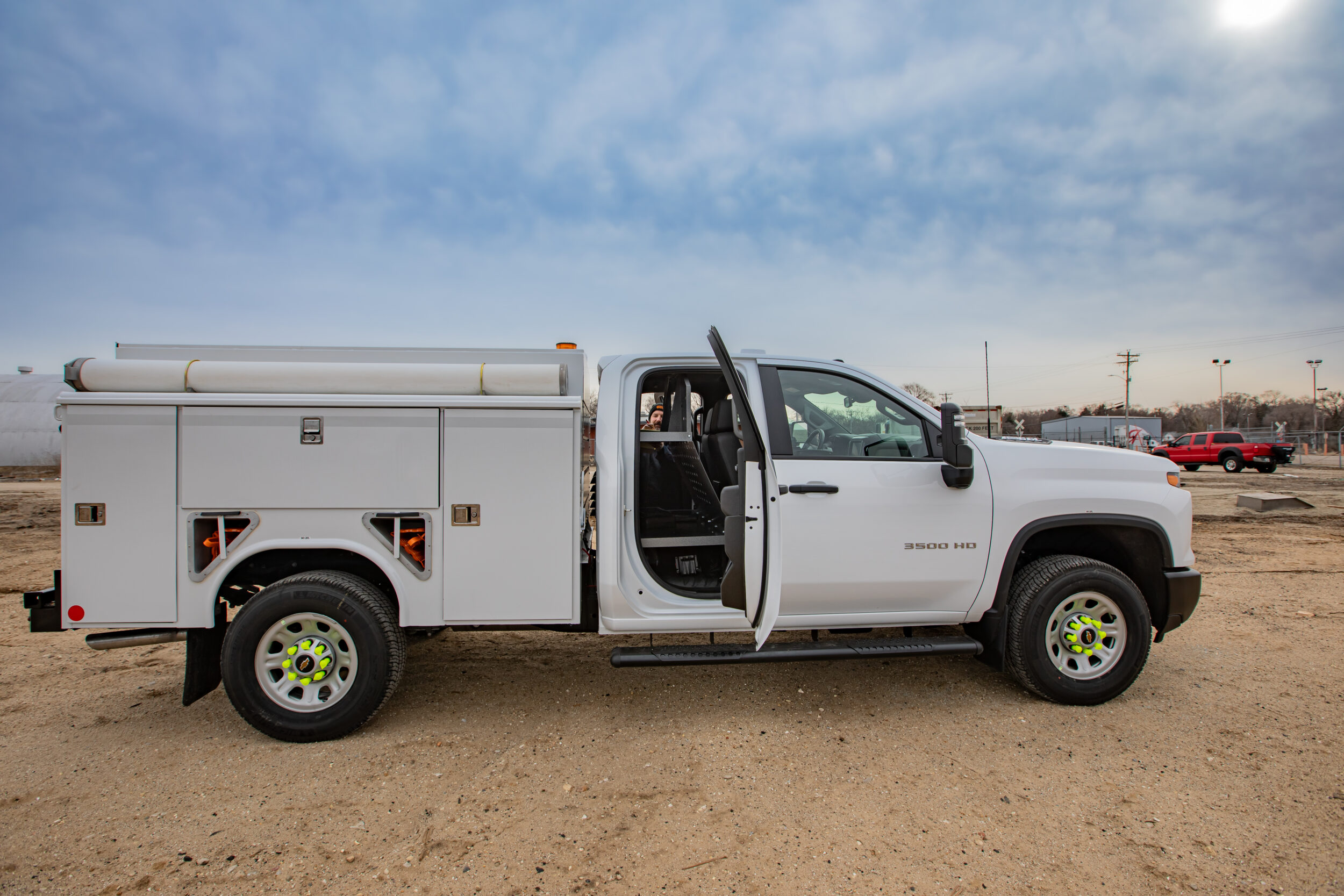 Side view of a white work truck that has the back door open and storage equipment in the back seat.